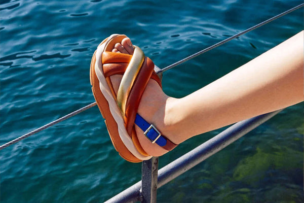 4CCCCEES Mellow Mela Women's Cross Strap Multi Color Sandal Lifestyle Leaning On Boat in Water Harry's Shoes Upper West Side NYC