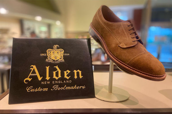 Alden Men's Leisure Handsewn 6243F Cap Toe Oxford Snuff Brown Suede Harry's Shoes Upper West Side  NYC Lifestyle, Shoe on Pedestal On Table Next To Alden Logo In Store